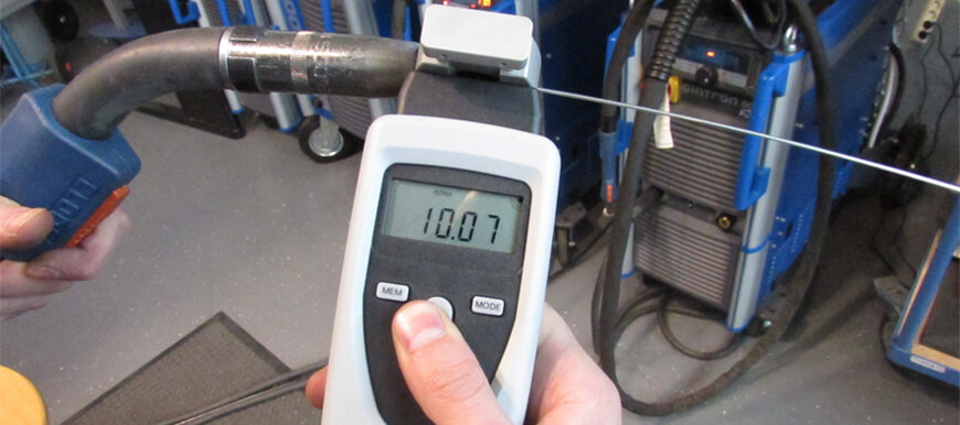Das Bild zeigt den Einsatz des digitalen Handtachometers rotaro Tw zur Validierung und Kalibrierung von Schweißgeräten in der Schweißindustrie. Der rotaro Tw wird mit einem Spezialadapter verwendet, um Schweißdrahtgeschwindigkeiten von 0,8 bis 3 mm Durchmesser zu messen.